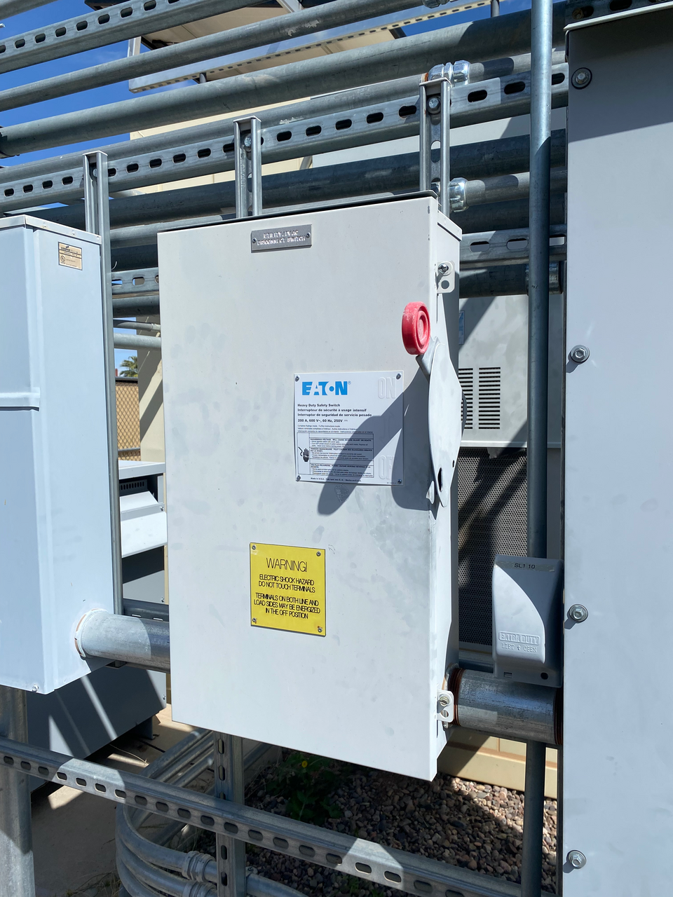A metal electrical disconnect switch box mounted on a wall, with a handle used to turn power on or off for a building.