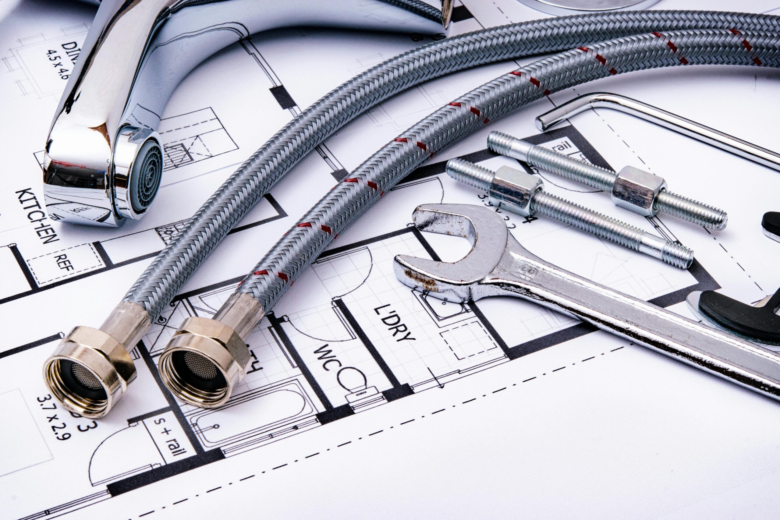 Close-up of plumbing tools and faucet on top of an architectural blueprint