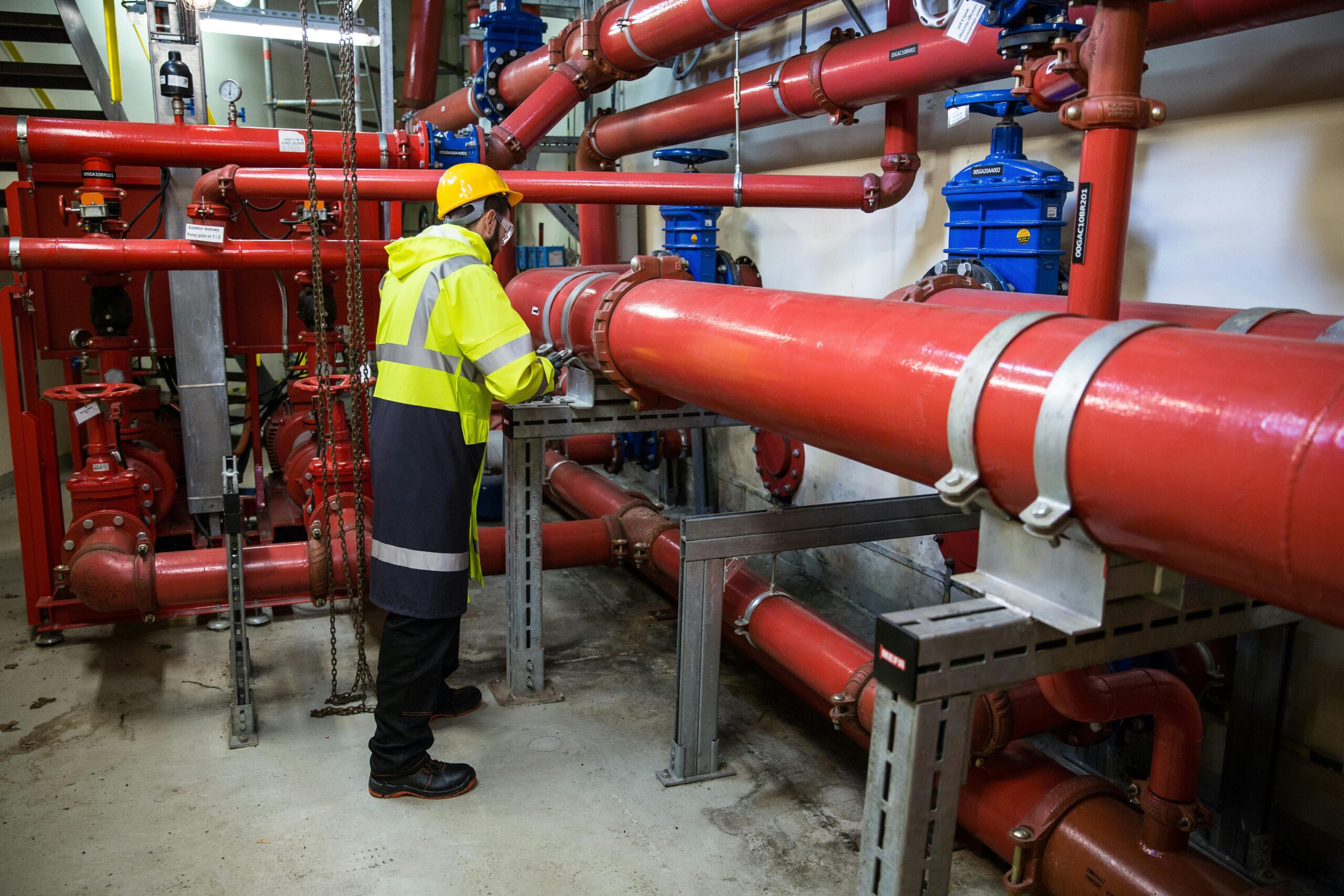 Engineer with safety gear inspecting red industrial piping system indoors